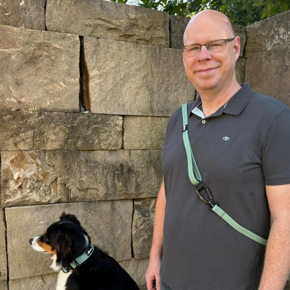 Mann mit grauem T-Shirt und Hund, der die WOOFLEX® Pro Führleine und ein grünes Geschirr trägt.