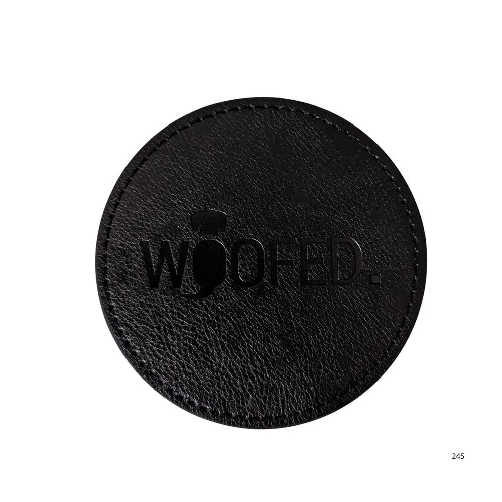 Runder, schwarzer Leder-Getränkeuntersetzer mit eingeprägtem "WOOFED." Schriftzug, schlichtes und elegantes Design.