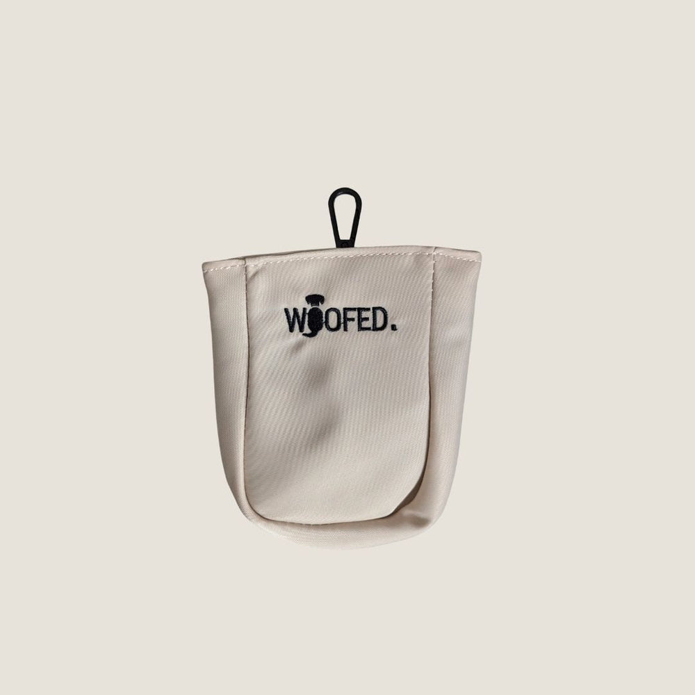 Beiger Leckerlibeutel mit schwarzem Schriftzug „WOOFED.“ und Schlaufe zur Befestigung für Gassitaschen.