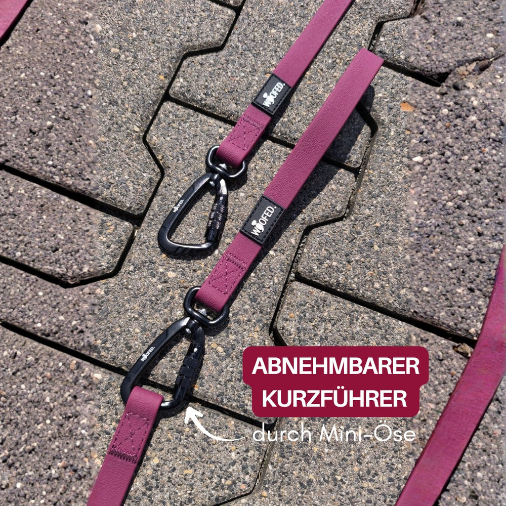 Lila WOOFLEX® Hundeleine mit abnehmbaren Kurzführer und Mini-Carabiner auf grauem Steinboden.