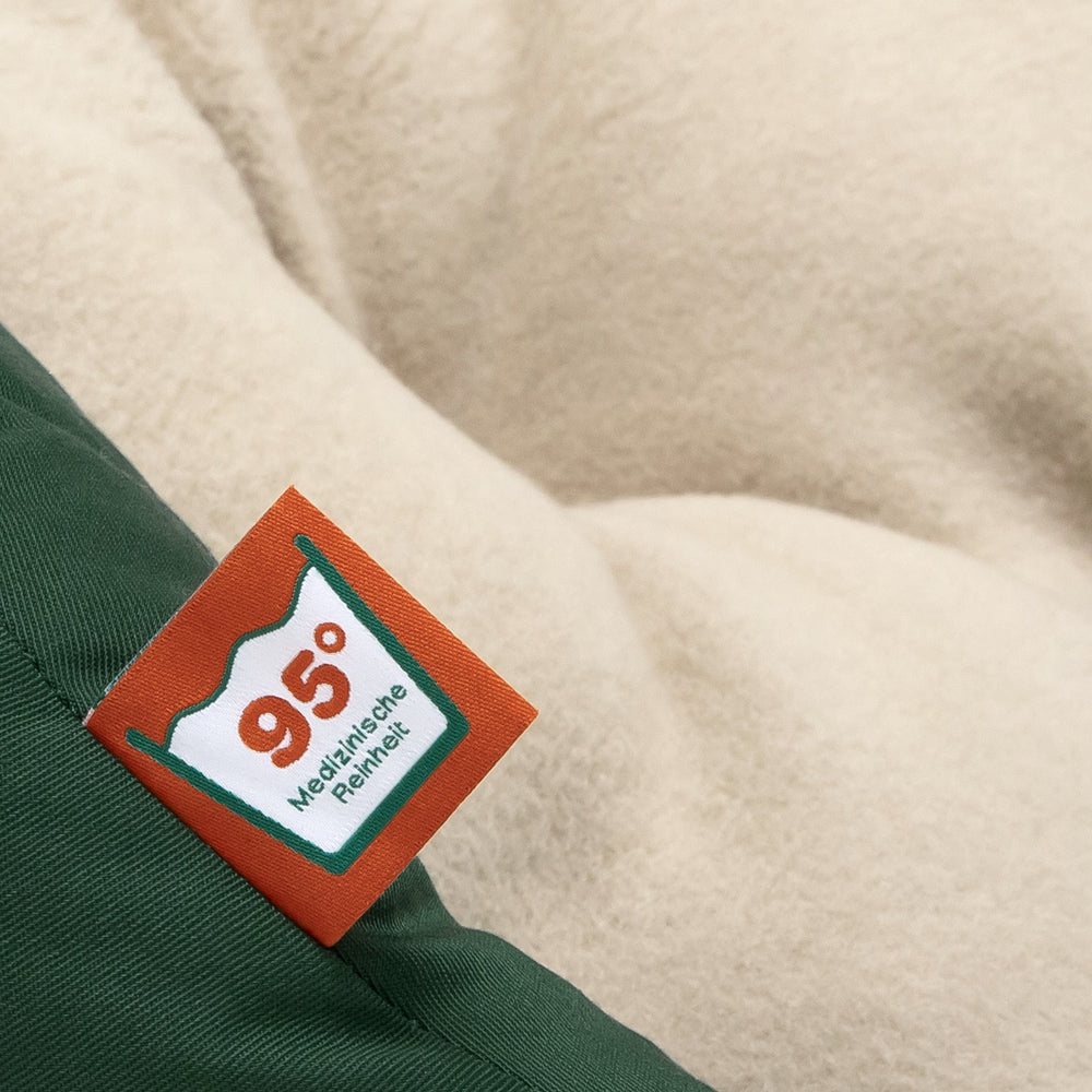 Gepolstertes Hundenest in Dunkelgrün und Beige mit orangefarbenem Etikett "95°" für besten Komfort.