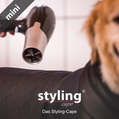 Hund im Styling-Cape mit Haartrockner, Schriftzug "styling" im Vordergrund, heller Hintergrund.