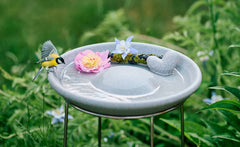 Vogeltränke Granicium auf Ständer, gefüllt mit Wasser, dekoriert mit Blume und Herz, kleiner Vogel am Rand.