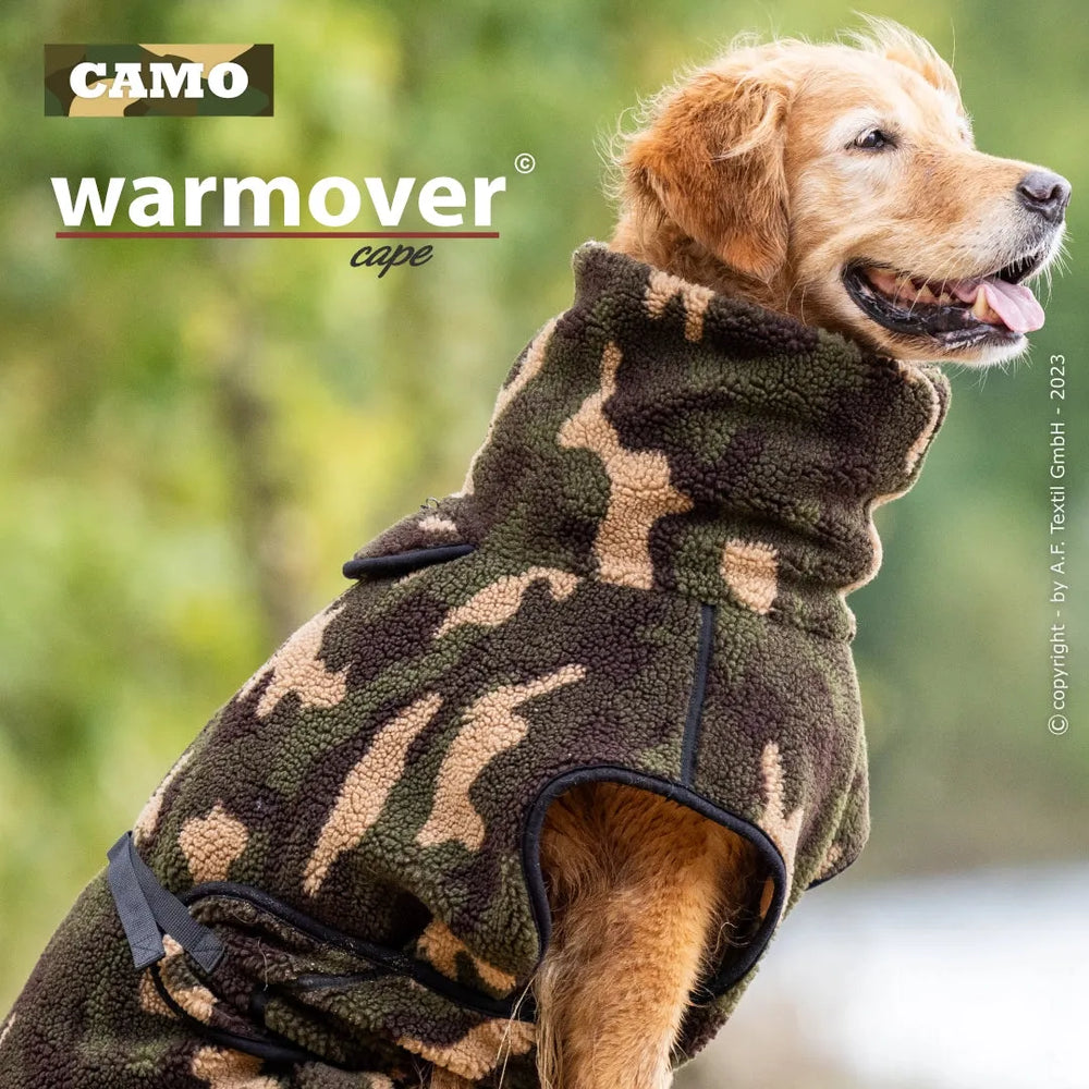 Hund im camouflagefarbenen Fleece-Mantel mit hohem Kragen, sitzt vor unscharfem Hintergrund.