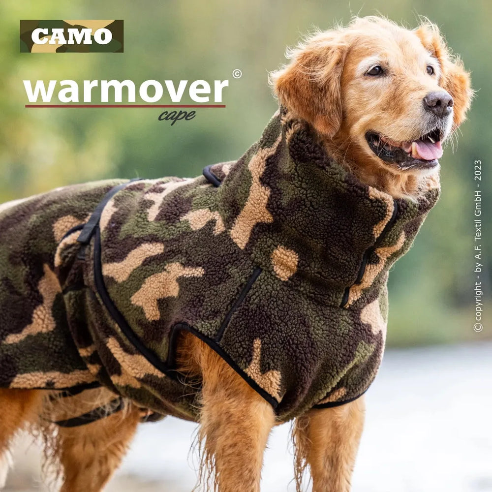 Hund im camouflagemusternden Wärmecape mit hohem Kragen vor unscharfem Naturhintergrund.