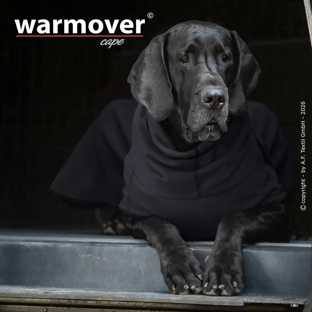 Schwarzer Hund in einem Wärmecape, entspannt sitzend am Fenster, mit dem Schriftzug "warmover cape" im Bild.