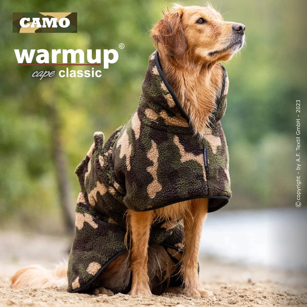 Hund trägt einen camouflaged Wende-Cape aus weichem Material, sitzt entspannt auf dem Boden.
