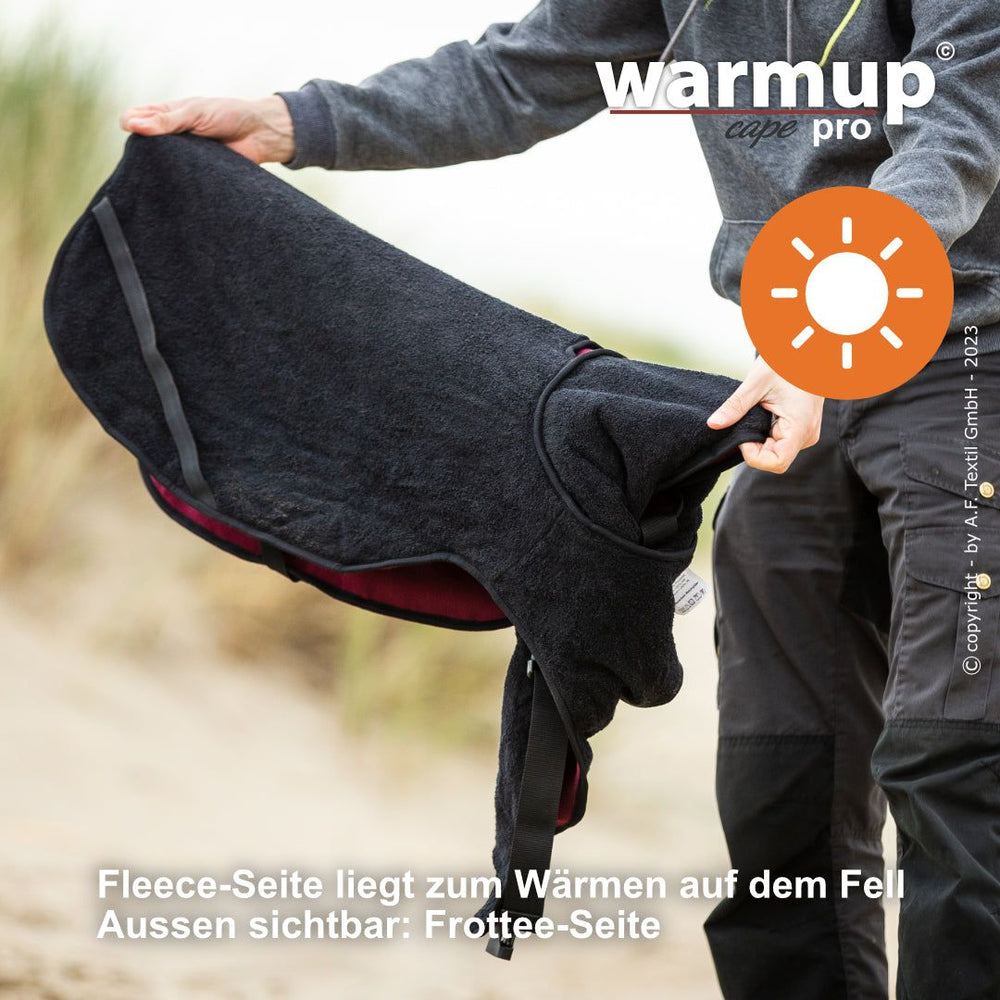 Person hält ein WARMUP© Wende-Cape in Schwarz und Bordeaux, erkennbar am "warmup pro"-Logo.