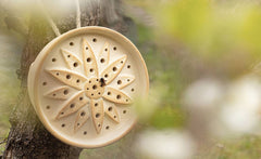 Wildbienenhaus in Blumenform aus Keramik, aufgehängt an einem Baum, mit Biene auf der Oberfläche.