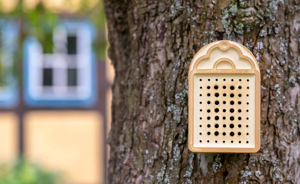 "Braunes Wildbienenhaus mit Nistlöchern, befestigt an einem Baum für sicheren Insektenschutz und Förderung der Biodiversität."