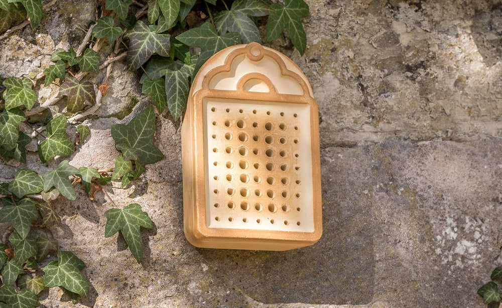 Braunes Insektenhotel mit Löchern zur Förderung von Wildbienen, befestigt an einer steinernen Wand.