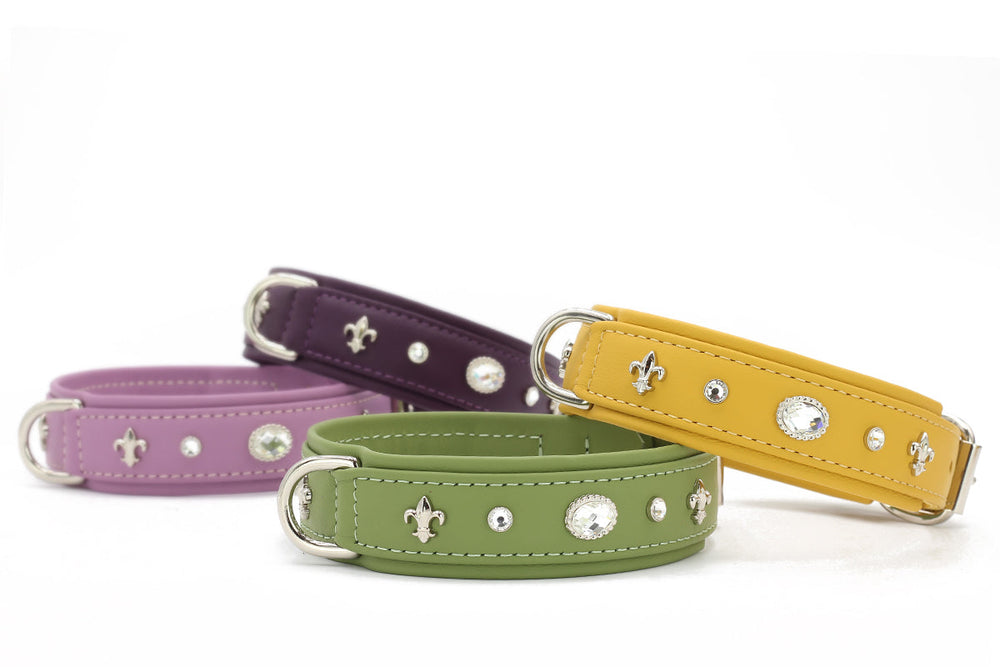 Verschiedene Hundehalsbänder in lila, dunkelgrün, gelb und violett mit Strasssteinen und Fleur-de-Lis-Muster.