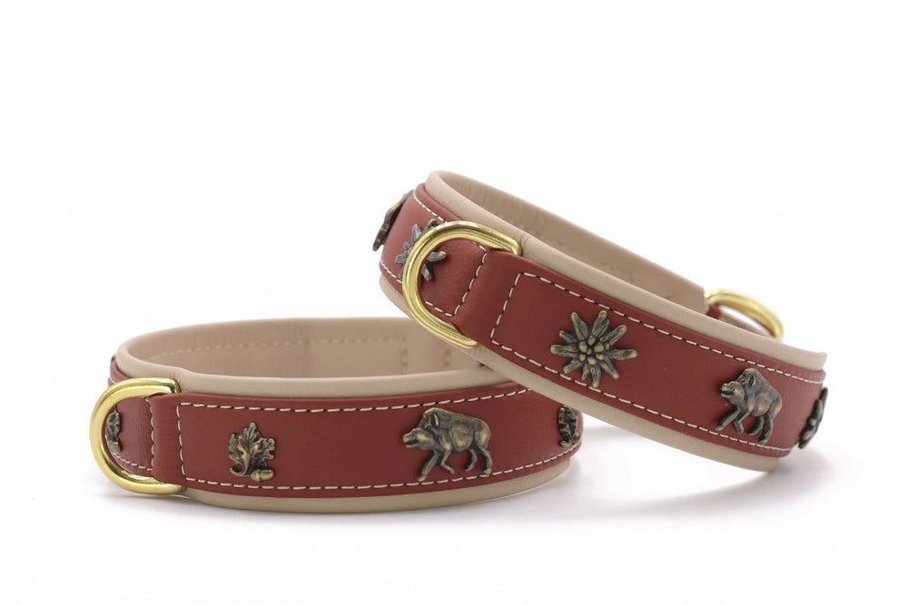 Zwei rot-braune Lederarmbänder mit goldfarbenen D-Ringen und dekorativen Tier- und Pflanzenmotiven.